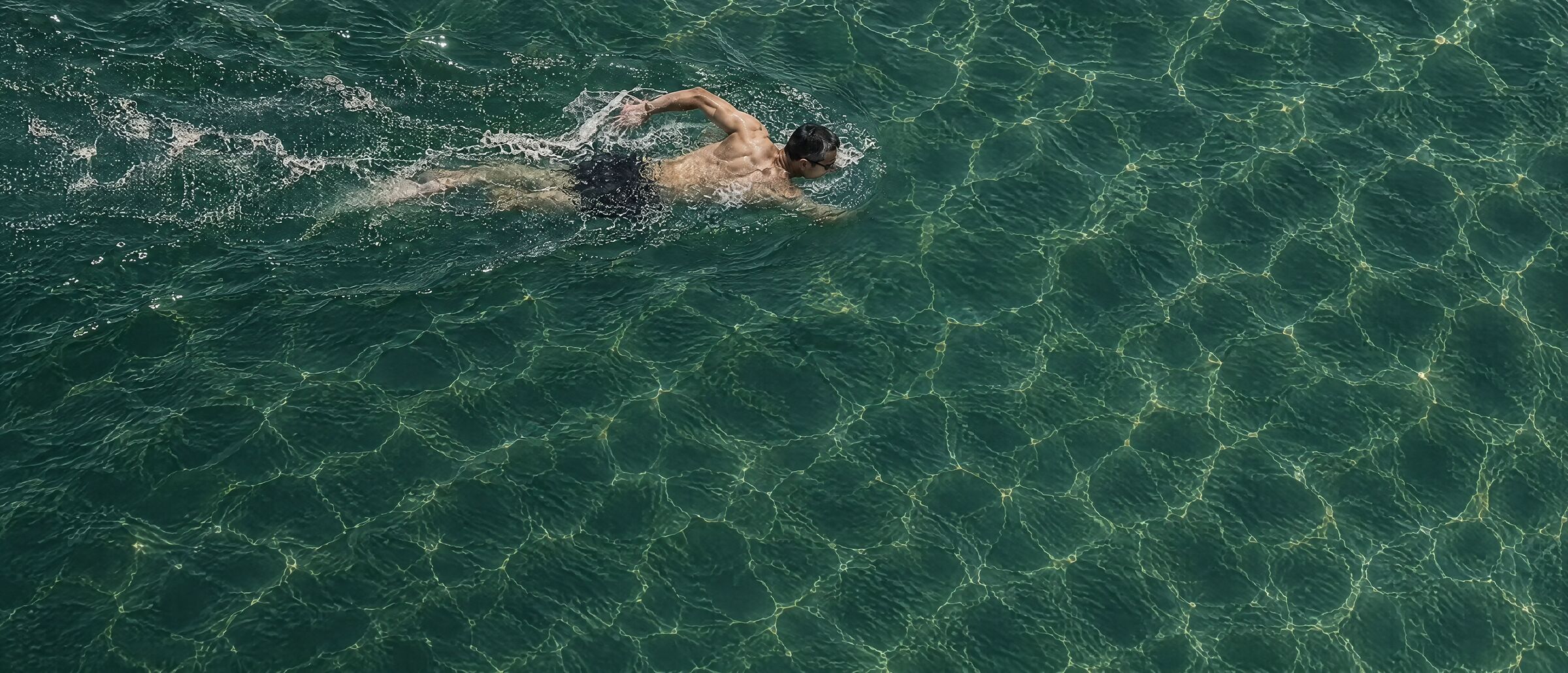 A swimmer mid-stroke in clear green water, seen from directly above